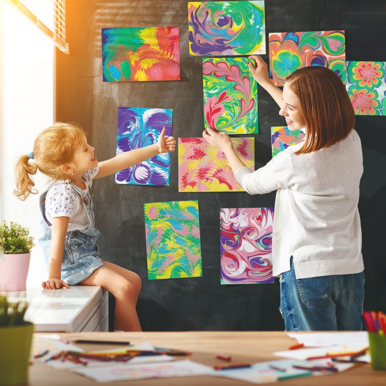 Mother and child girl hang their drawings on the wall